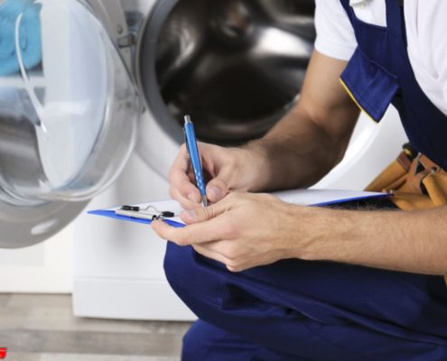 main crouching down near a washing machine with a pen and clipboard - Appliance Solutions appliance maintenance