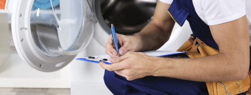 main crouching down near a washing machine with a pen and clipboard - Appliance Solutions appliance maintenance