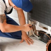 man wearing a blue hat and blue overalls fixing an appliance - Appliance Solutions appliance repair