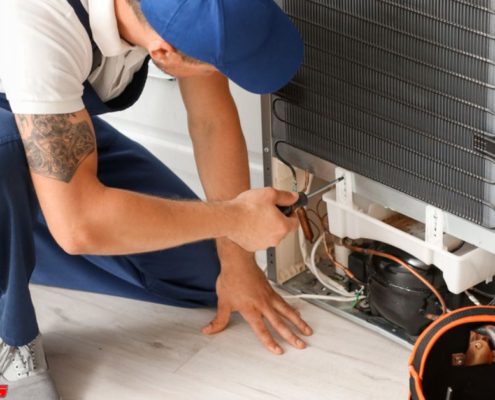 man wearing a blue hat and blue overalls fixing an appliance - Appliance Solutions appliance repair
