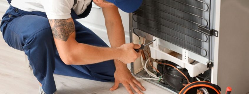man wearing a blue hat and blue overalls fixing an appliance - Appliance Solutions appliance repair
