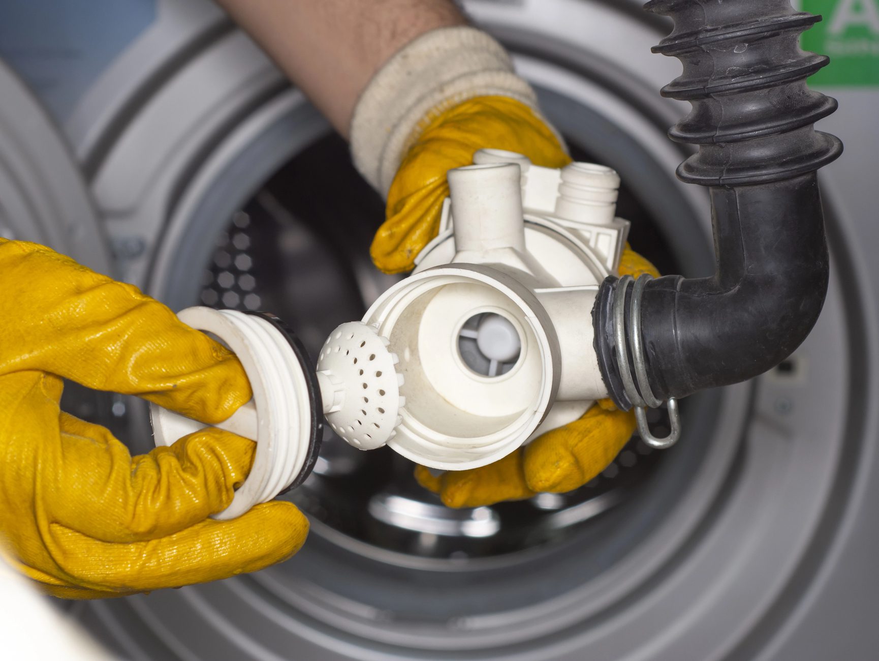 Appliance-Solutions-Ham-Lake-MN-Appliance-Parts repair man fixing a washing machine while holding a white and black plastic part - Appliance Solutions
