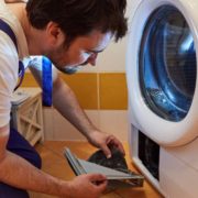 man wearing blue overalls fixing a white dryer - Appliance Solutions dryer repair