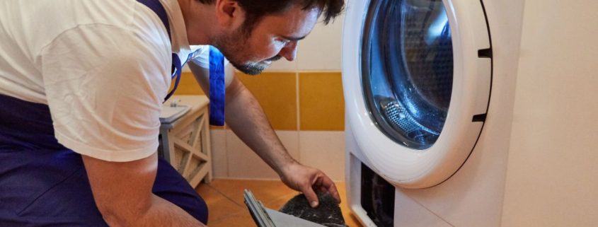 man wearing blue overalls fixing a white dryer - Appliance Solutions dryer repair
