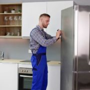 man wearing blue overalls fixing a stainless steel fridge - Appliance Solutions In Stock Appliance Parts Near Blaine MN
