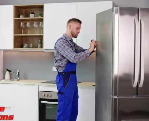 man wearing blue overalls fixing a stainless steel fridge - Appliance Solutions In Stock Appliance Parts Near Blaine MN