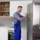 man wearing blue overalls fixing a stainless steel fridge - Appliance Solutions In Stock Appliance Parts Near Blaine MN