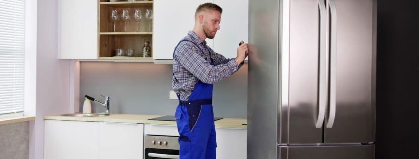 man wearing blue overalls fixing a stainless steel fridge - Appliance Solutions In Stock Appliance Parts Near Blaine MN