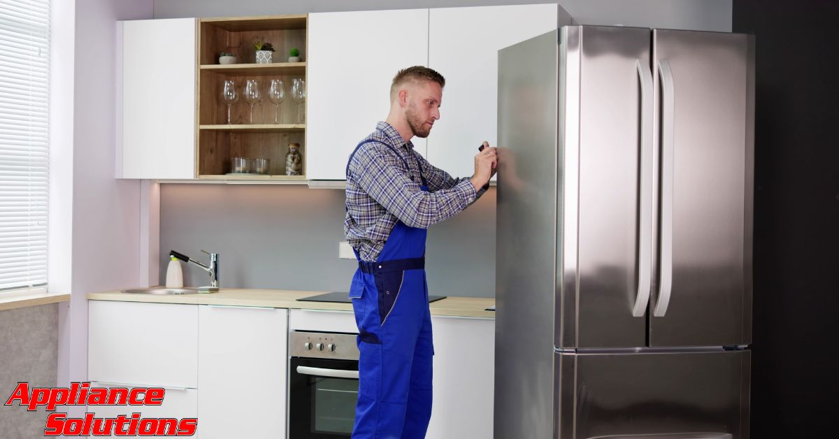 man wearing blue overalls fixing a stainless steel fridge - Appliance Solutions appliance repair