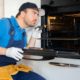 repair man sitting next to open oven - Appliance Solutions oven repair