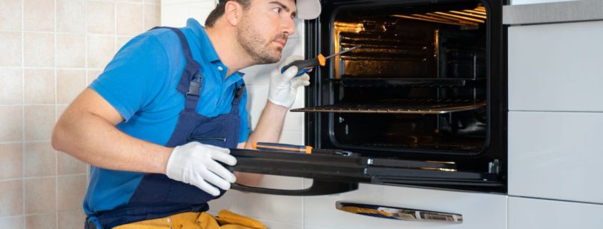 repair man sitting next to open oven - Appliance Solutions oven repair