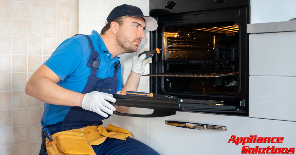 repair man sitting next to open oven - Appliance Solutions appliance service