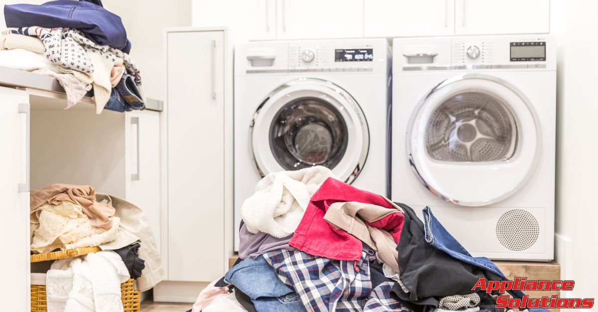 piles of dirty laundry by a washer and dryer - Appliance Solutions washing machine repair